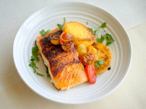 round plate with salmon, cherry tomatoes, and polenta cakes