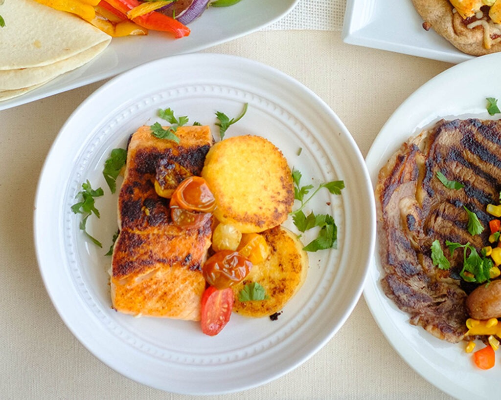 round plate with salmon, cherry tomatoes, and polenta cakes