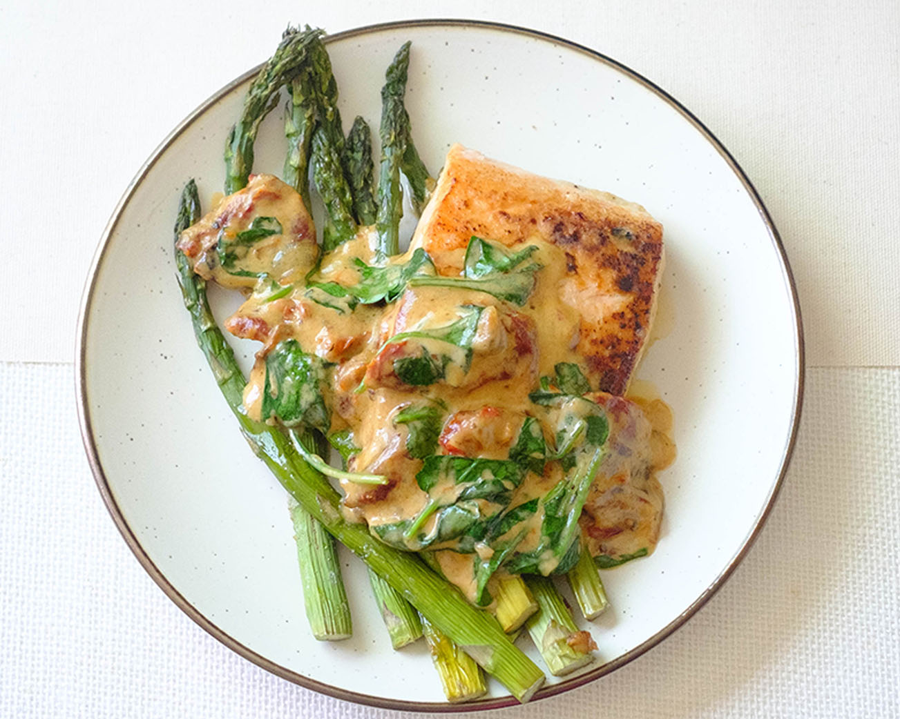 round plate with salmon with creamy sun-dried tomato sauce and asparagus