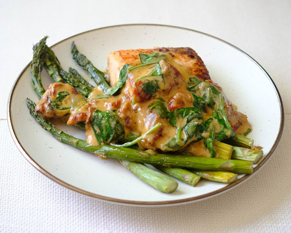 round plate with salmon with creamy sun-dried tomato sauce and asparagus