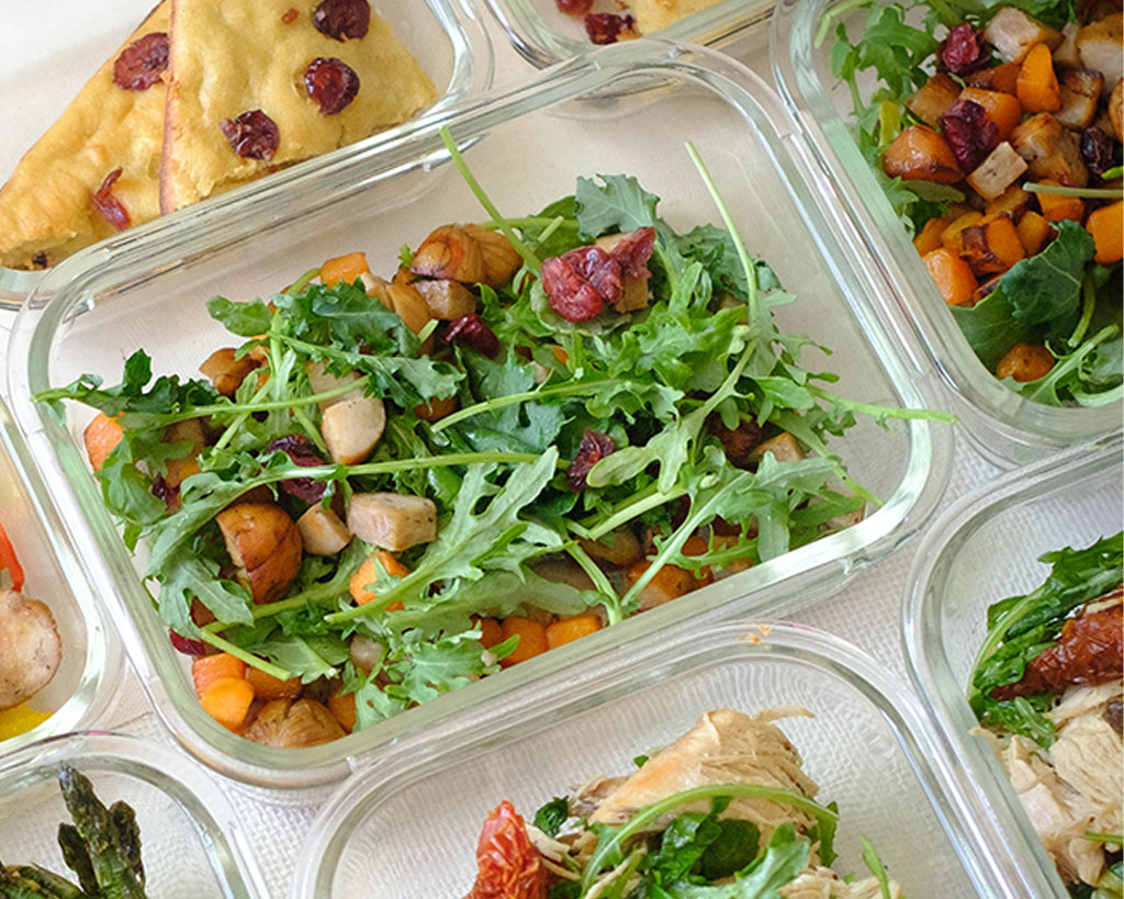 Glass meal prep container with diced sausage, diced butternut squash, dried cranberries, and green arugula salad.