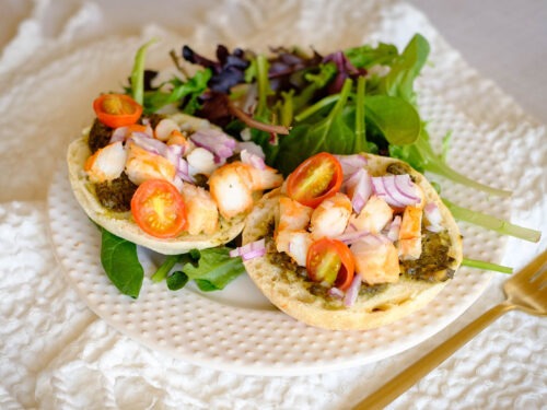 round plate with english muffins topped with chopped shrimp, red onions, and cherry tomatoes with spring mix salad