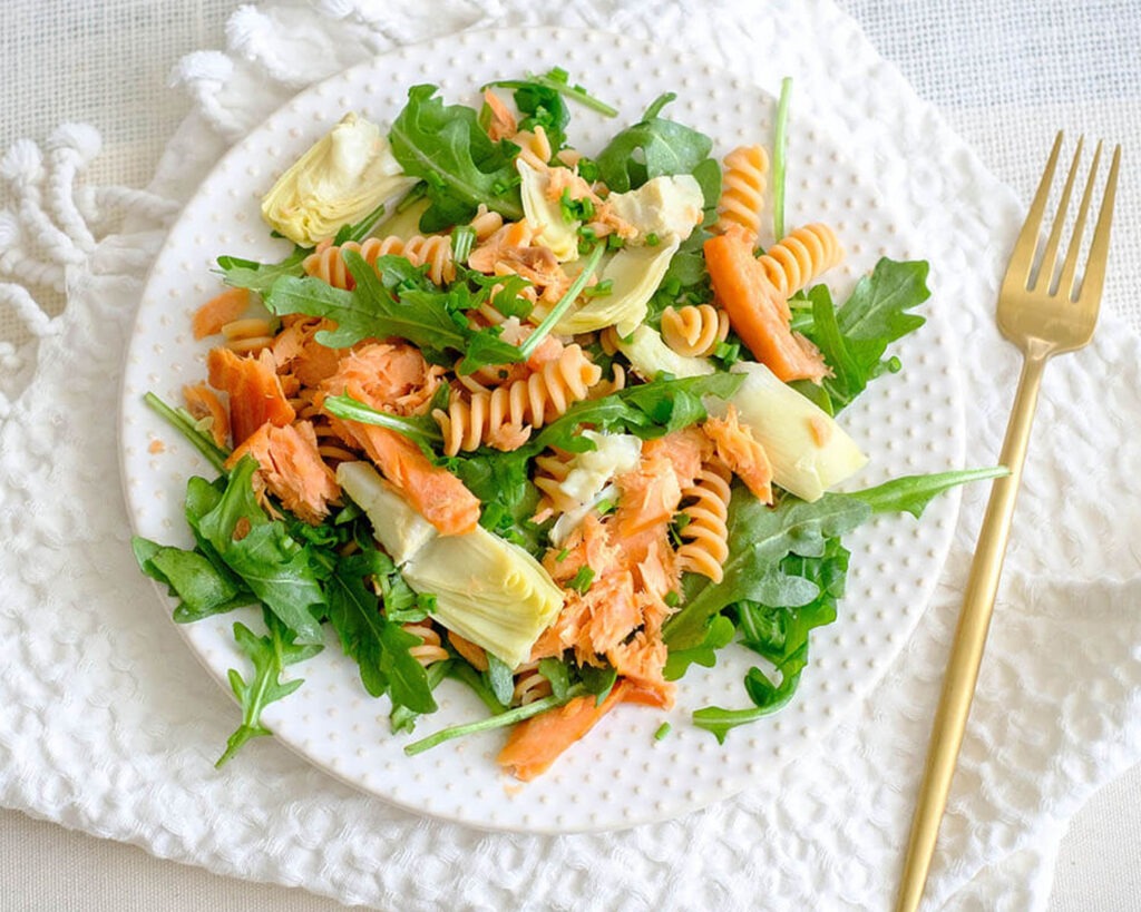 round plate with rotini pasta, smoked salmon, artichoke hearts, and arugula