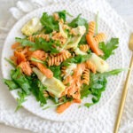 round plate with rotini pasta, smoked salmon, artichoke hearts, and arugula