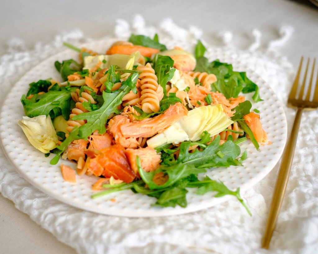 round plate with rotini pasta, smoked salmon, artichoke hearts, and arugula