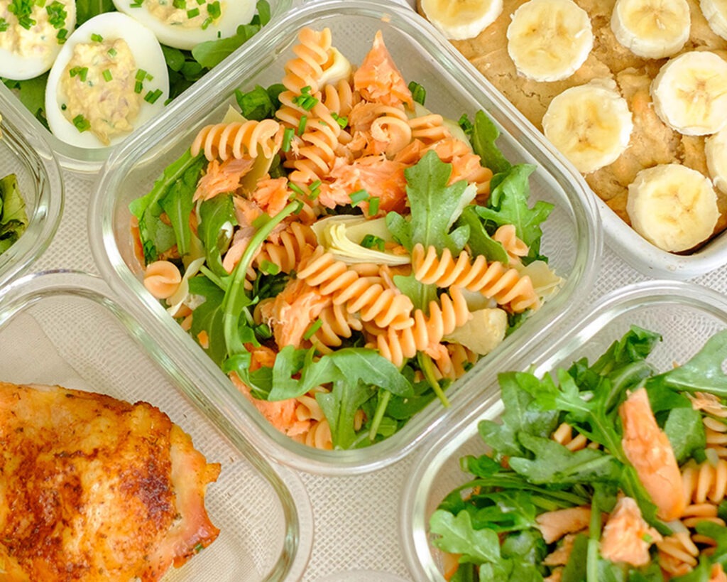 glass meal prep containers with rotini pasta, smoked salmon, artichoke hearts, and arugula