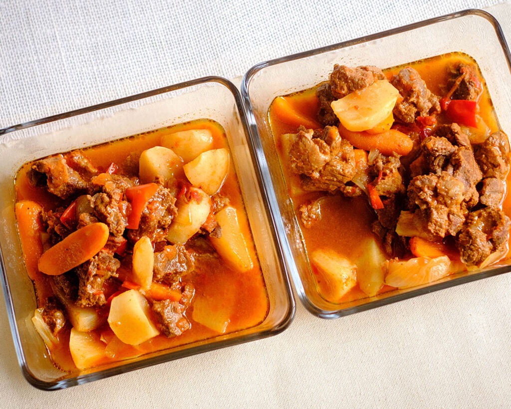 glass meal prep containers with beef stew, carrots, and turnips
