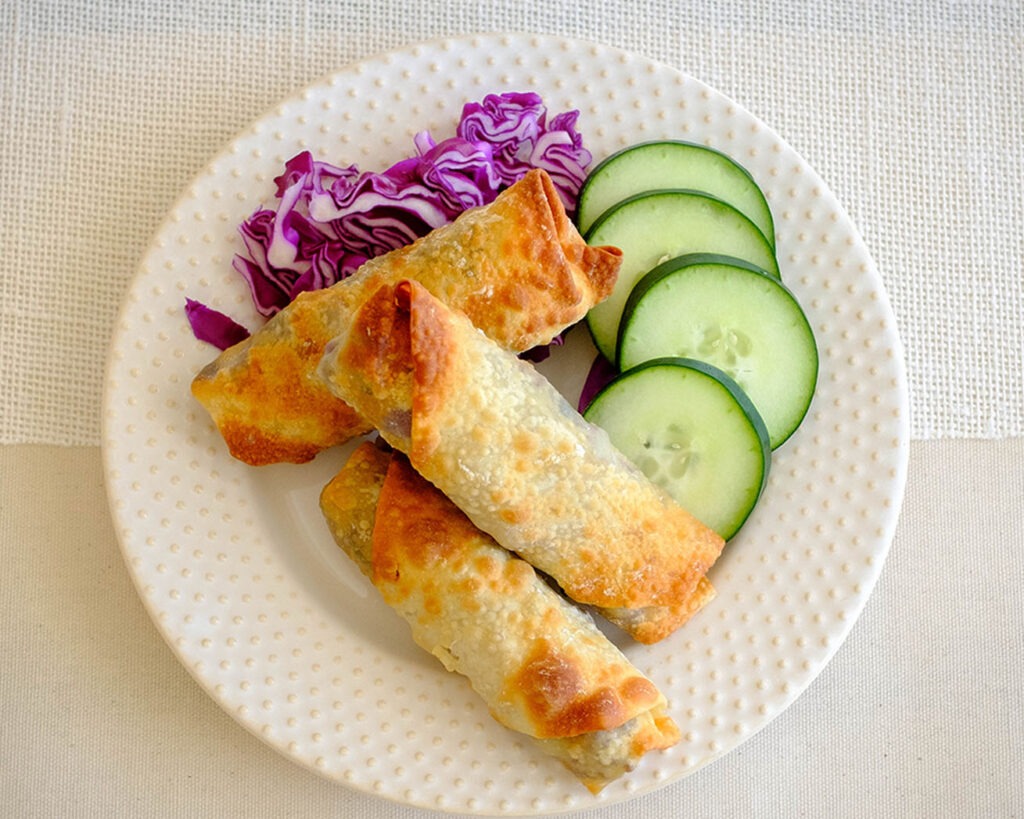 round plate with egg rolls, sliced green cucumber, and shredded red cabbage