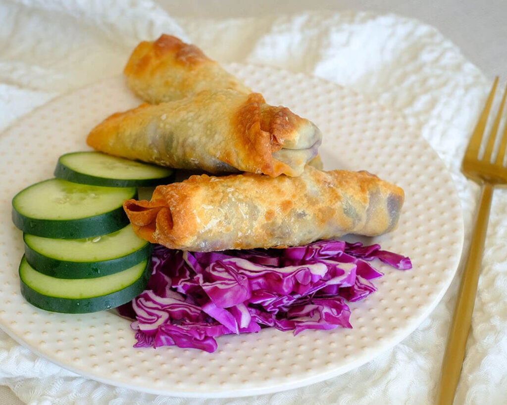 round plate with egg rolls, sliced green cucumber, and shredded red cabbage