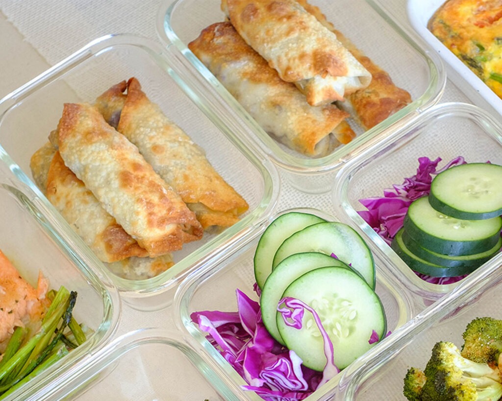 glass meal prep containers with egg rolls, sliced green cucumber, and shredded red cabbage