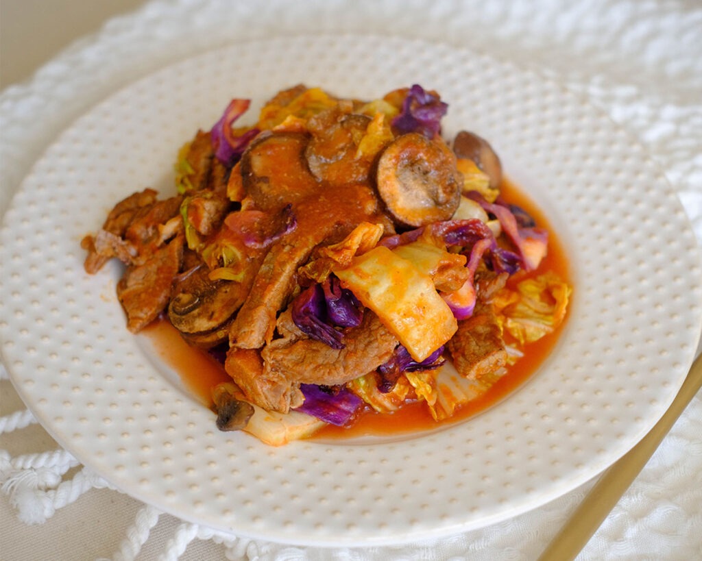 round plate with beef chunks in tomato sauce with napa cabbage, red cabbage, and sliced mushrooms