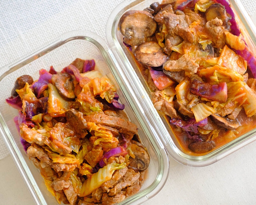 glass meal prep containers with beef chunks in tomato sauce with napa cabbage, red cabbage, and sliced mushrooms