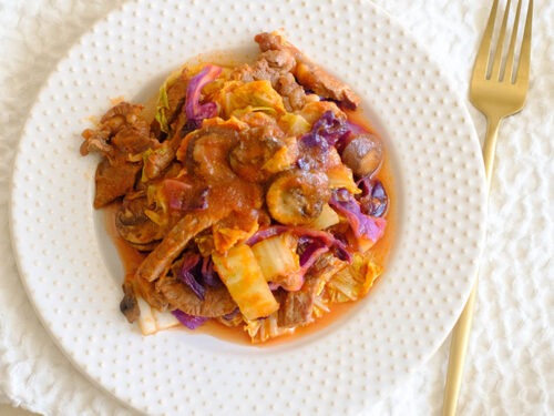 round plate with beef chunks in tomato sauce with napa cabbage, red cabbage, and sliced mushrooms