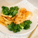 Round white plate with pan-fried fish, baked potato wedges and green kale