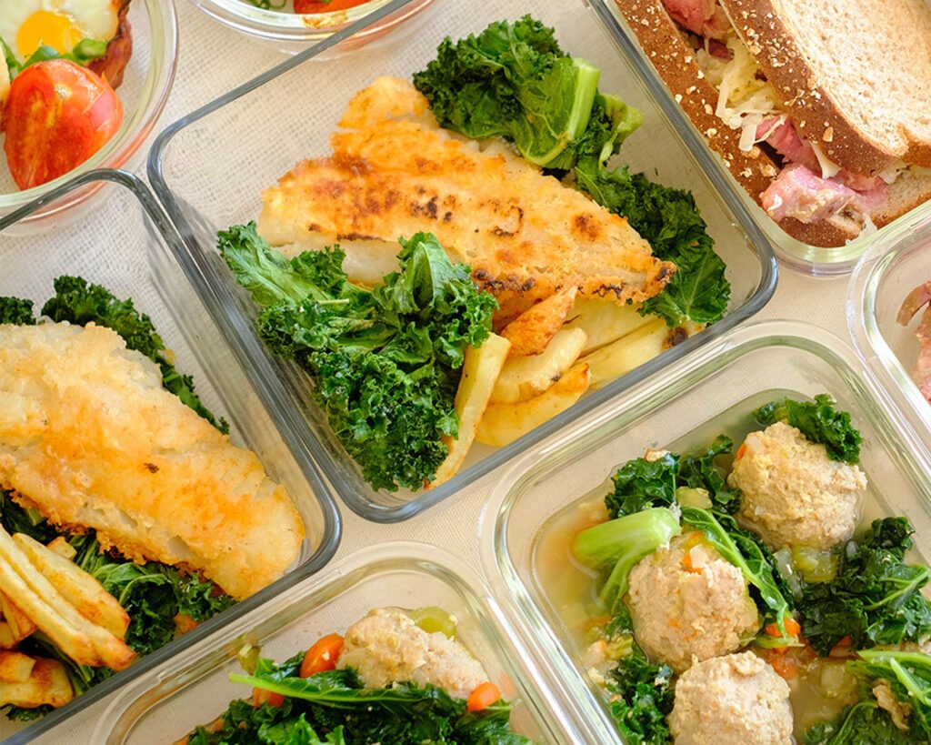 Square glass meal prep containers with pan-fried fish, baked potato wedges and green kale