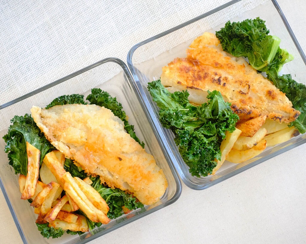 Square glass meal prep containers with pan-fried fish, baked potato wedges and green kale