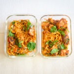 glass meal prep containers with pasta and pumpkin marinara with green spinach and shredded cheese