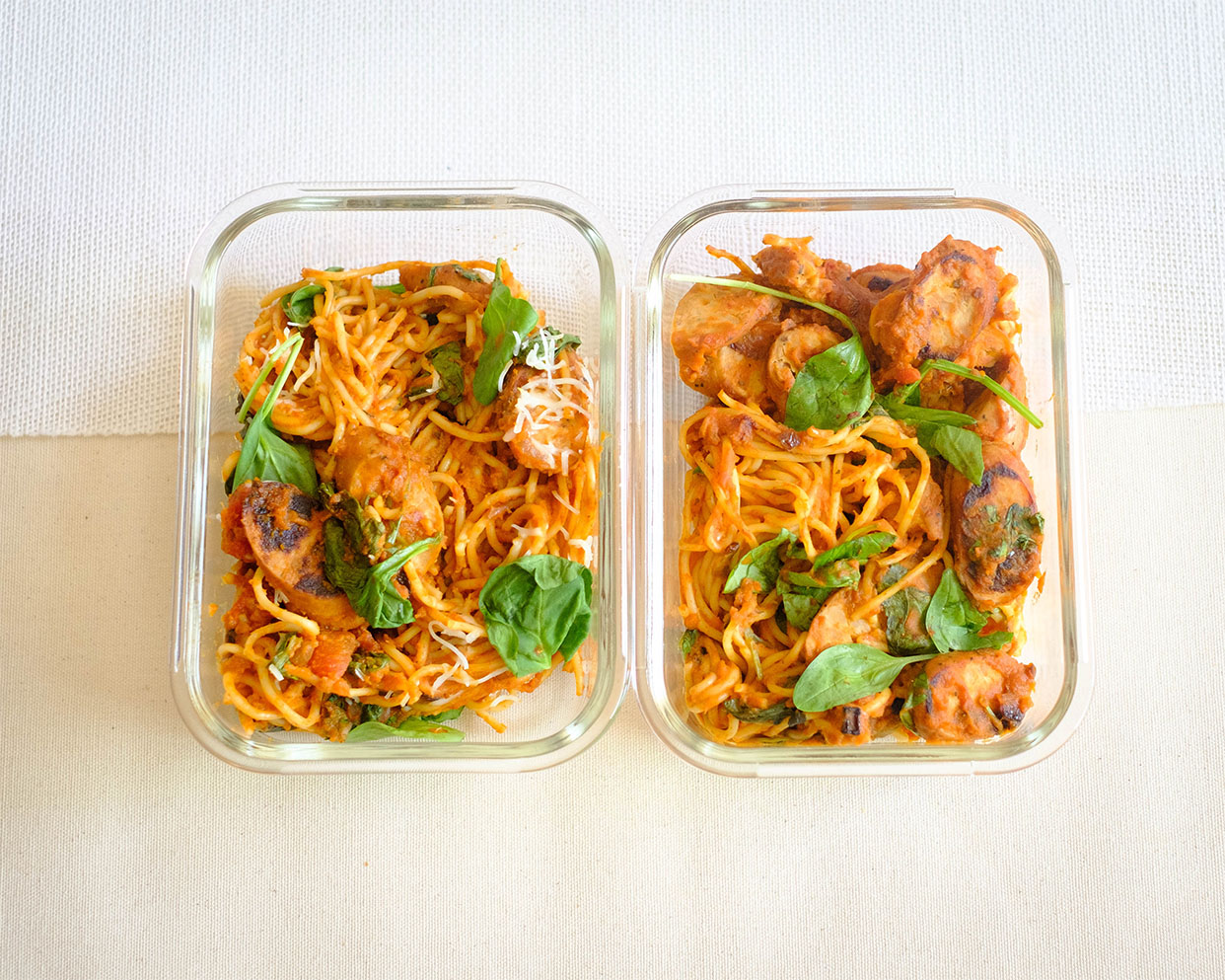 glass meal prep containers with pasta and pumpkin marinara with green spinach and shredded cheese
