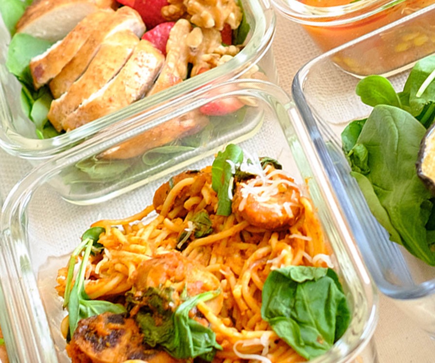 glass meal prep container with pasta and pumpkin marinara with green spinach and shredded cheese