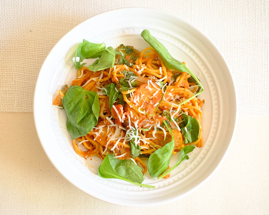 round plate with pasta and pumpkin marinara with green spinach and shredded cheese