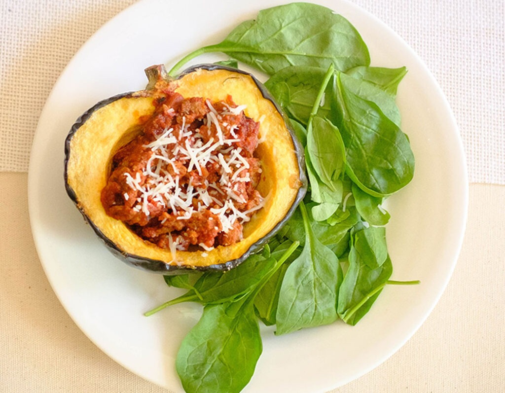 round plate with acorn squash stuffed with beef marinara sauce and green baby spinach