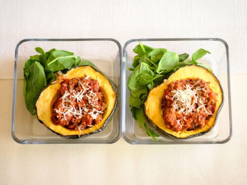 glass meal prep containers with acorn squash stuffed with beef marinara sauce and green baby spinach