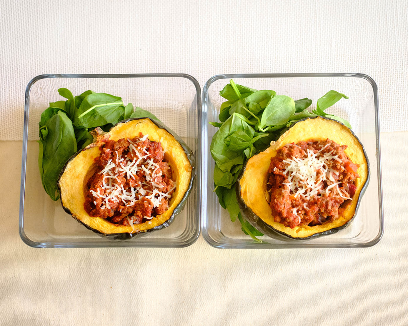 glass meal prep containers with acorn squash stuffed with beef marinara sauce and green baby spinach