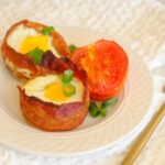 round plate with bacon wrapped eggs and roasted tomato