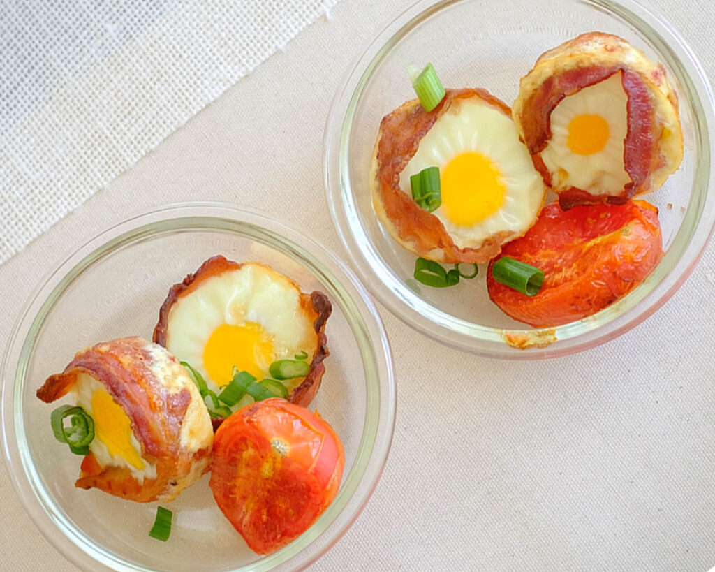 round glass meal prep containers with bacon wrapped eggs and roasted tomato
