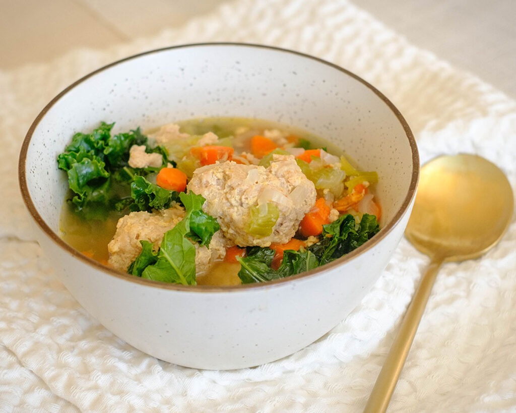 round bowl with chicken meatball soup, diced carrots, celery, onions, and baby kale