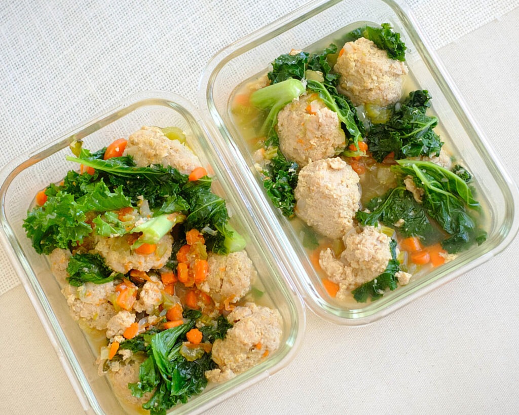 glass meal prep containers with chicken meatball soup, diced carrots, celery, onions, and baby kale