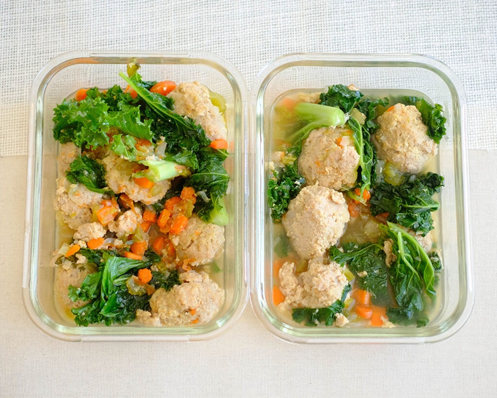 glass meal prep containers with chicken meatball soup, diced carrots, celery, onions, and baby kale