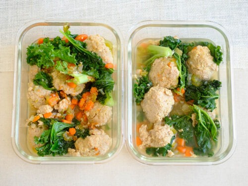 glass meal prep containers with chicken meatball soup, diced carrots, celery, onions, and baby kale
