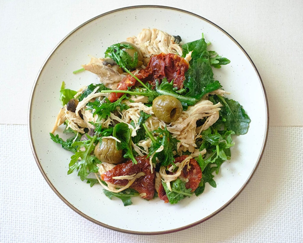 round plate with shredded chicken, sun-dried tomato, green olives, and baby kale