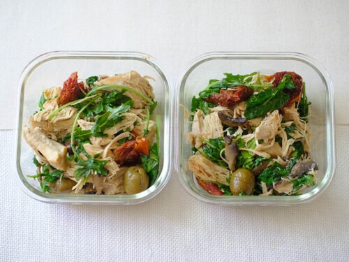 glass meal prep containers with shredded chicken, sun-dried tomato, green olives, and baby kale