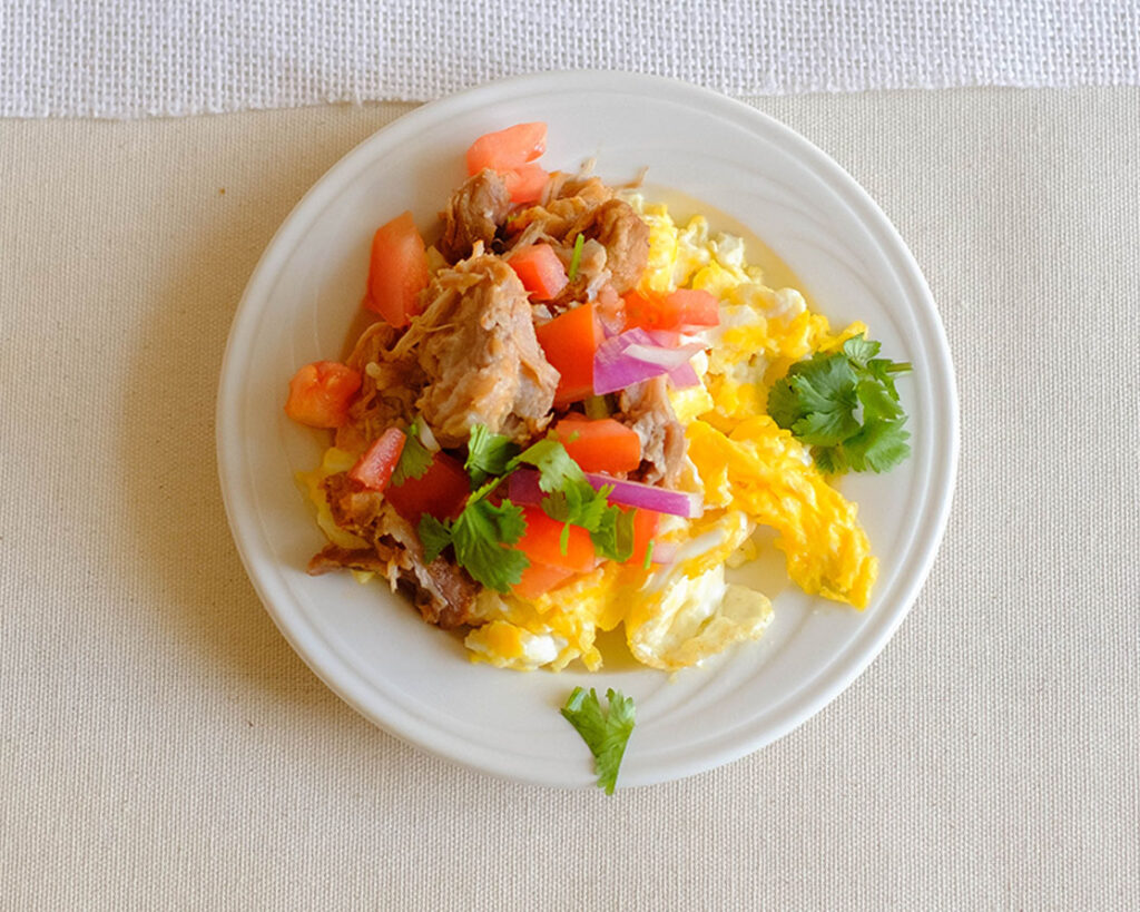 round plate with scrambled eggs, shredded pork, tomatoes, cilantro, and onions
