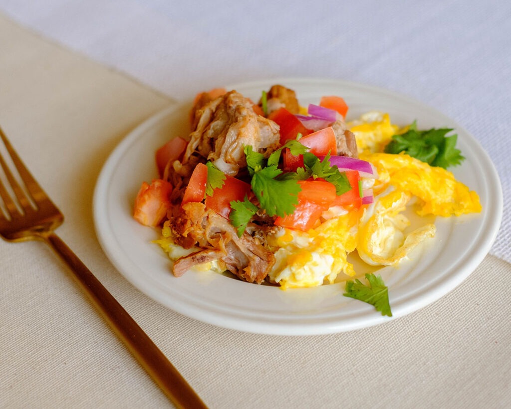 round plate with scrambled eggs, shredded pork, tomatoes, cilantro, and onions