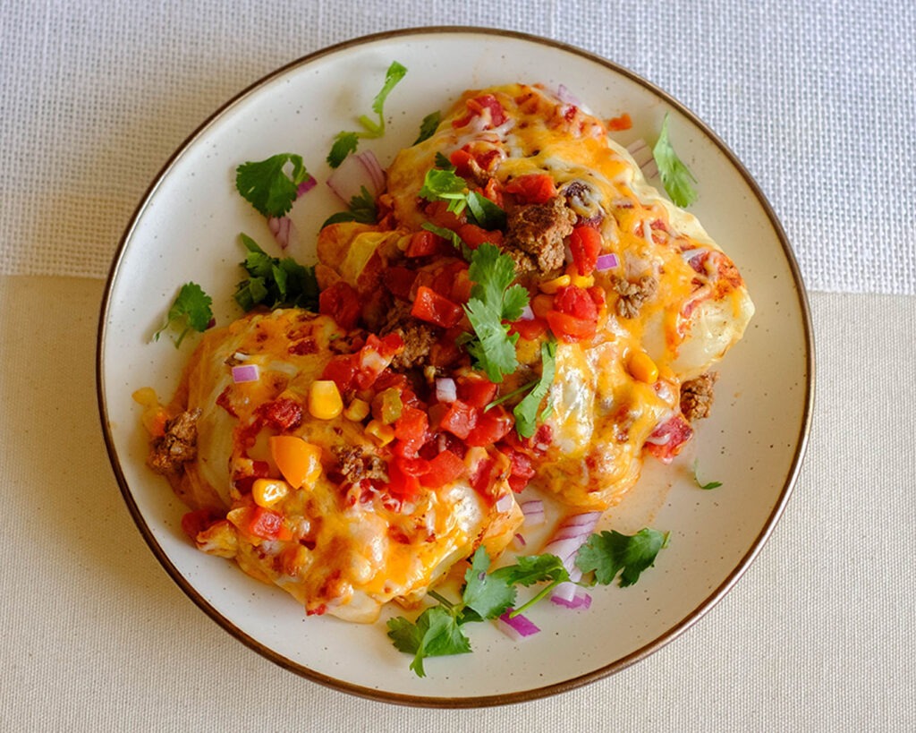 round plate with mexican cabbage roll topped with shredded cheese, diced tomatoes, and corn