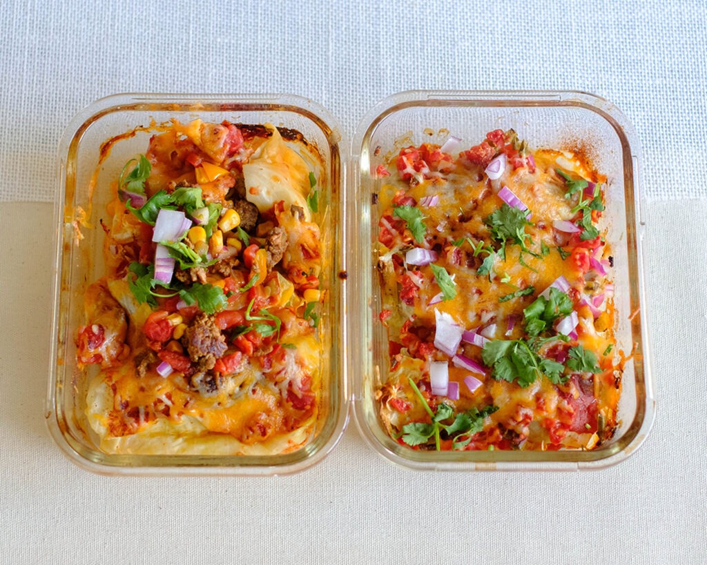 glass meal prep containers with mexican cabbage roll topped with shredded cheese, diced tomatoes, and corn