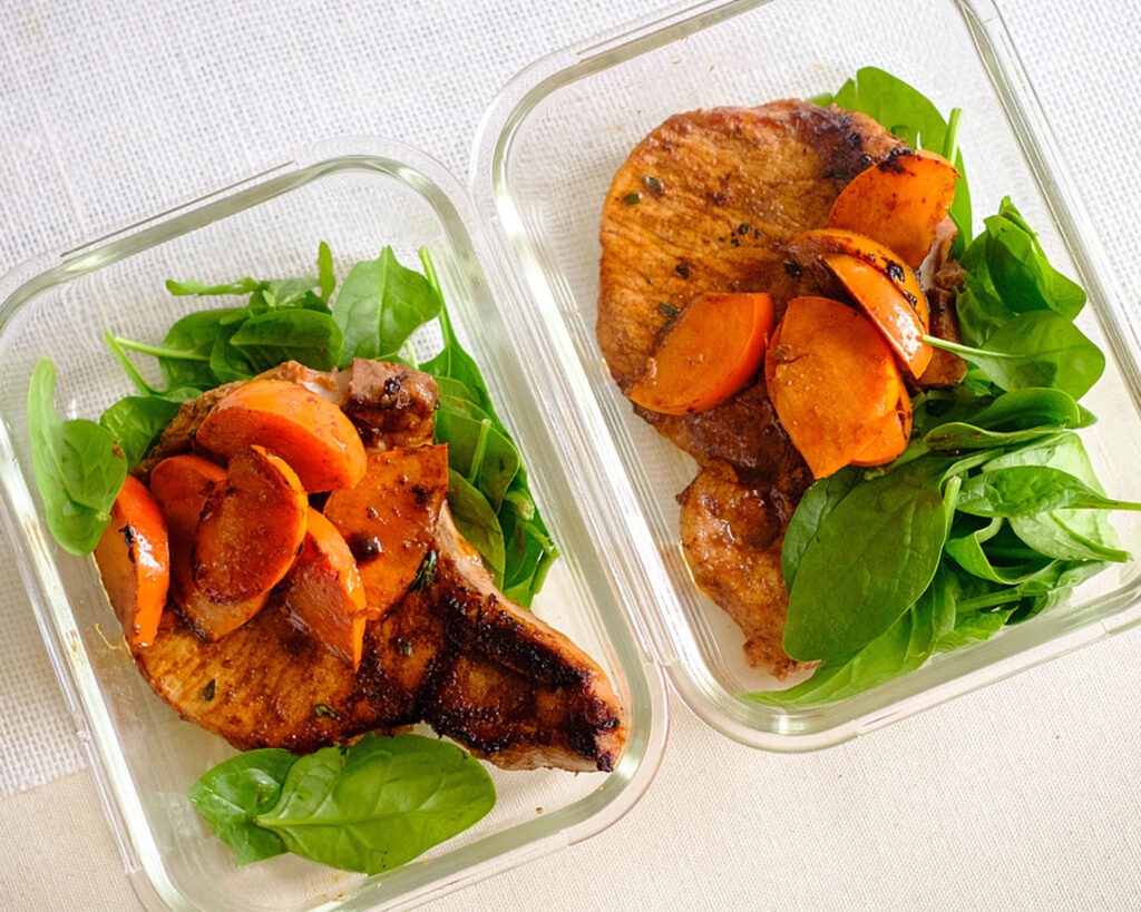 glass meal prep containers with pork meal prep of balsamic glazed porkchops with persimmons and baby spinach