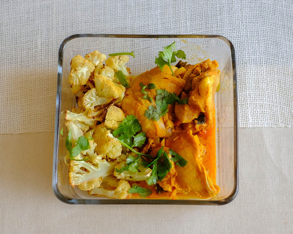 square glass meal prep container with instant pot butter chicken and roasted cauliflower