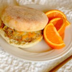 round plate with english muffin with a sausage patty, topped with shredded cheese and orange slices.