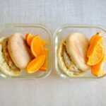 glass meal prep containers with english muffin with a sausage patty, topped with shredded cheese and orange slices.