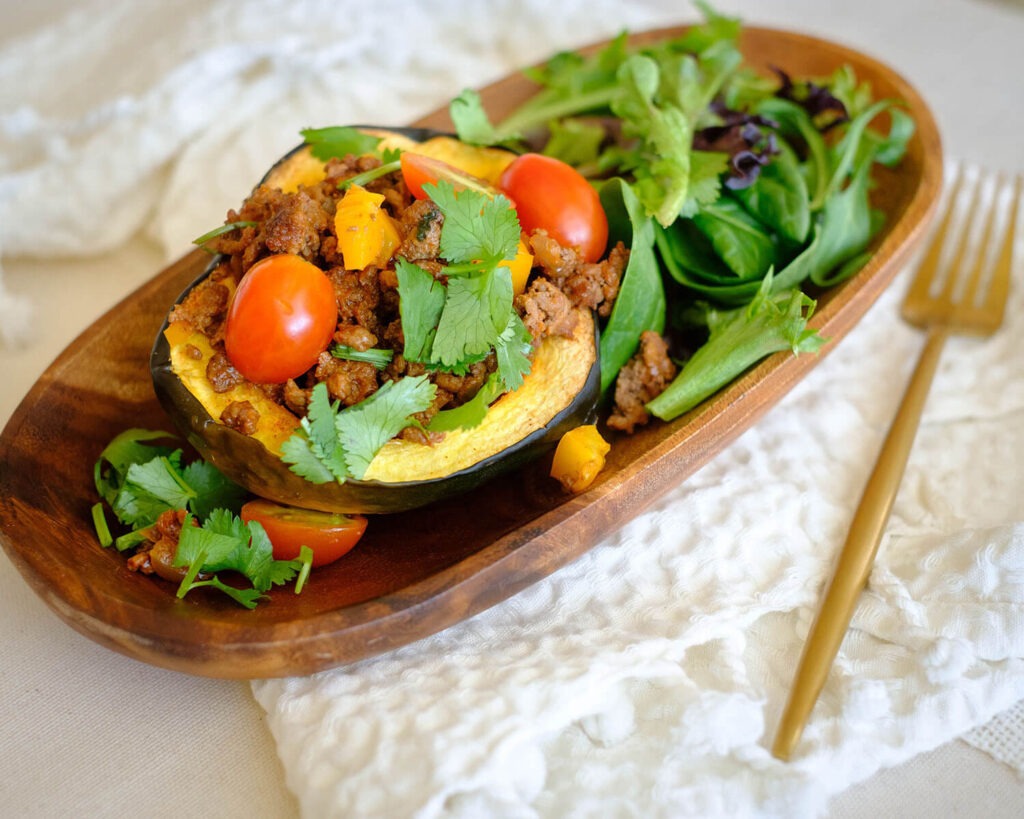 wooden plate with acorn squash stuffed with taco meat, tomatoes, and side spring salad