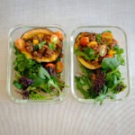 rectangle meal prep container with acorn squash stuffed with taco meat, tomatoes, and side spring salad