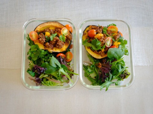 rectangle meal prep container with acorn squash stuffed with taco meat, tomatoes, and side spring salad