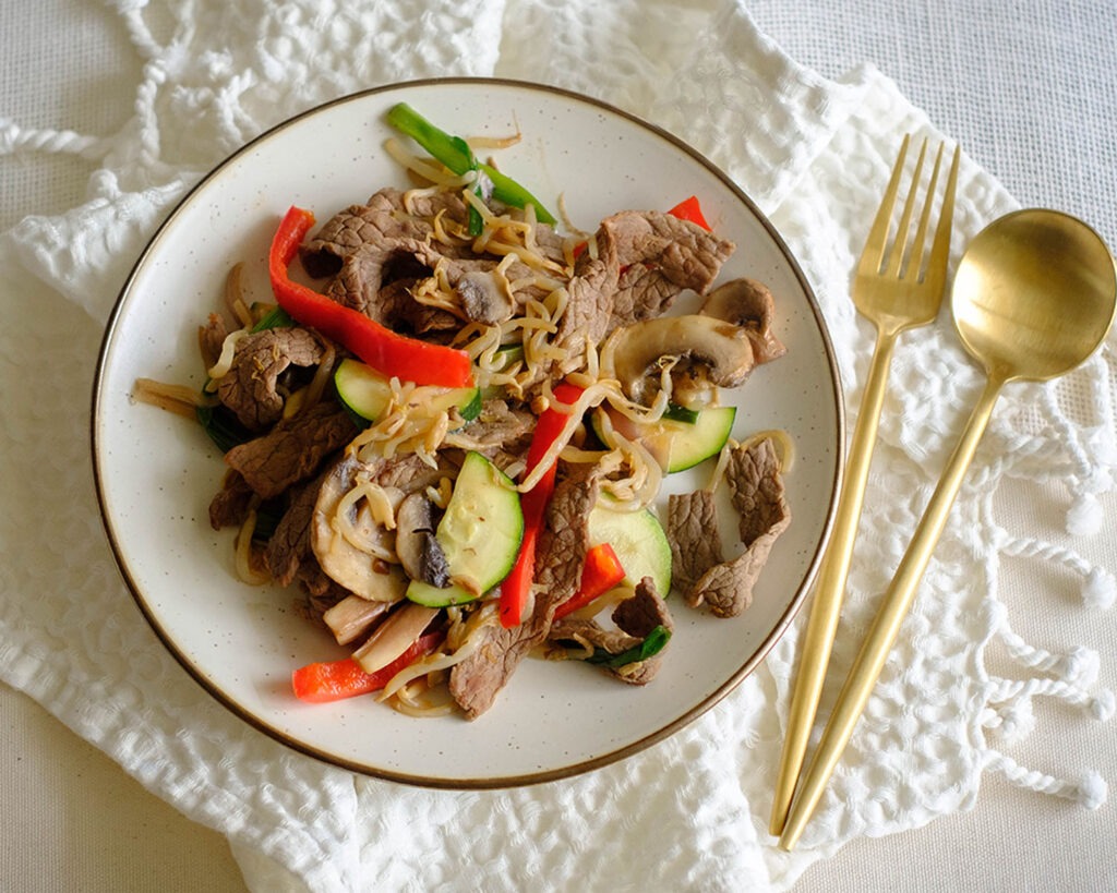 round plate with weekly meal prep of sliced beef stir fry with bell peppers, sliced zucchini, and sliced mushrooms, and bean sprouts