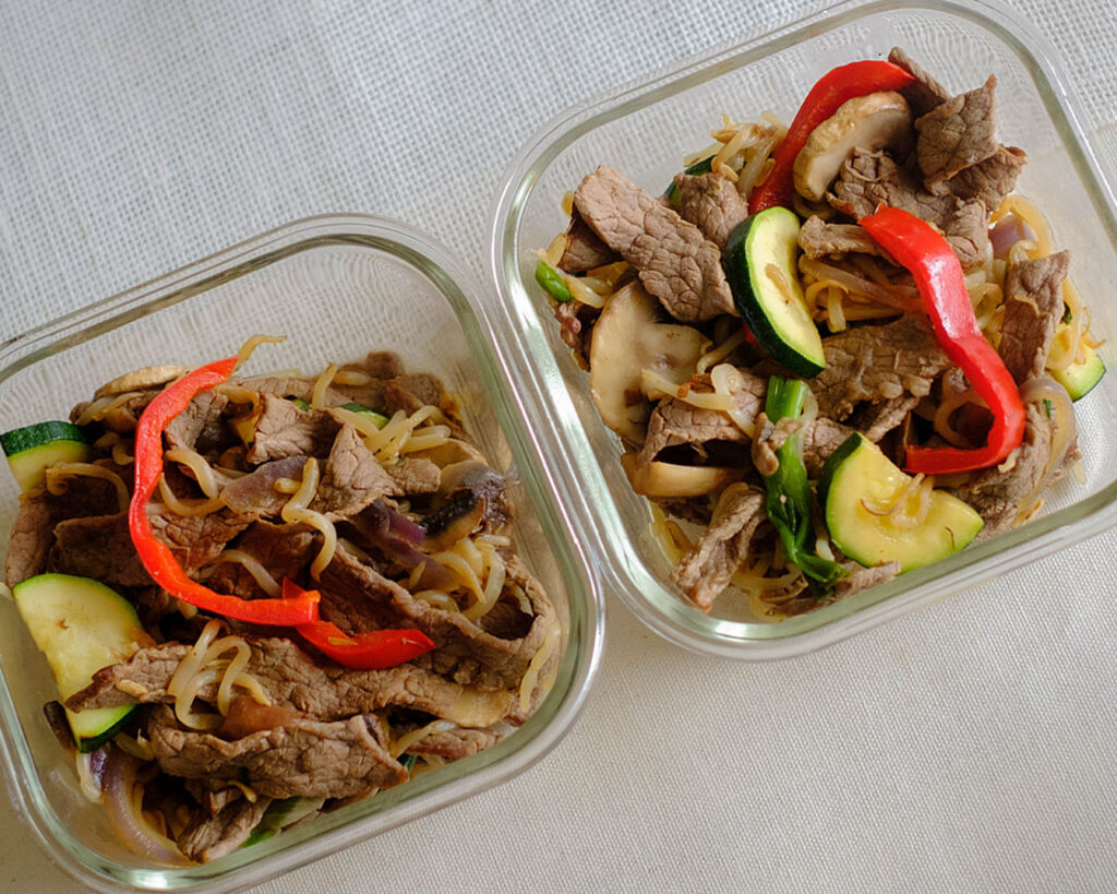 glass square containers with sliced beef stir fry with bell peppers, sliced zucchini, and sliced mushrooms, and bean sprouts for weekly meal prep