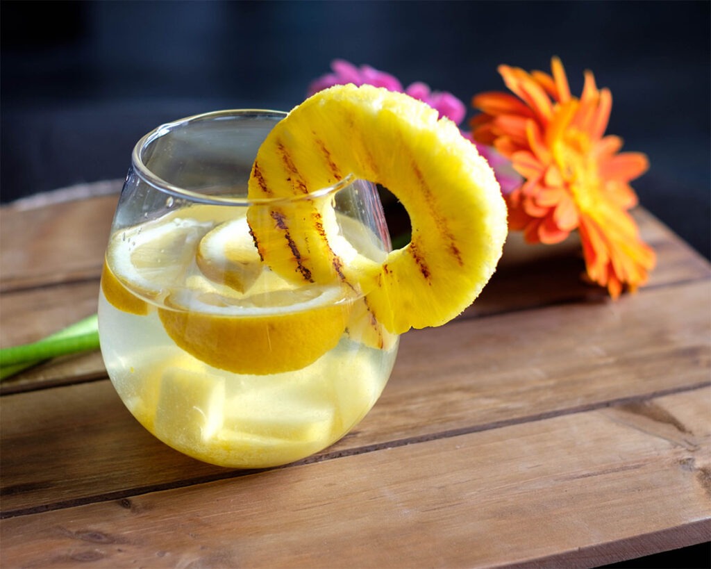 glass of water with lemon slices and a pineapple ring for hydration tips
