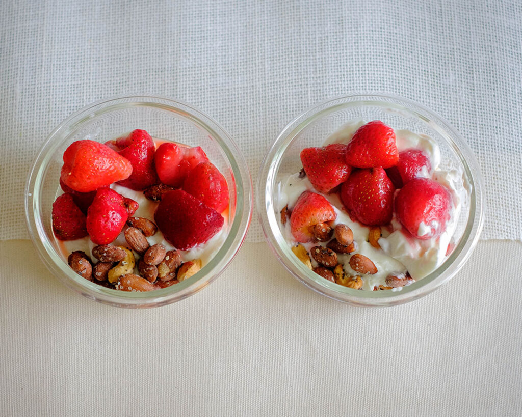 round glass containers with yogurt topped with strawberries and mixed nuts for a healthy breakfast